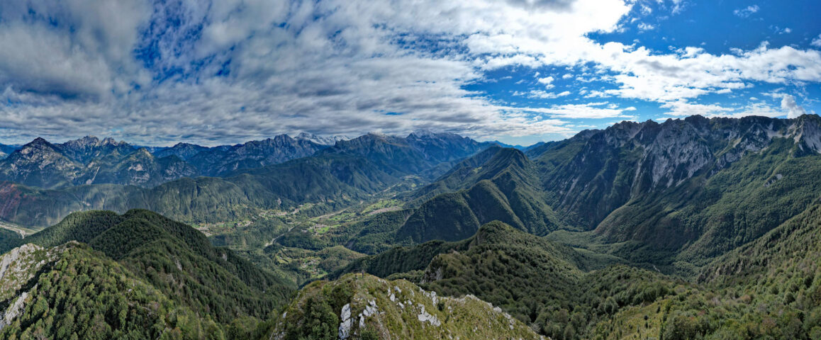 Veduta panoramica della Val Resia, con rilievi montuosi, valli verdi e cielo parzialmente nuvoloso sopra le Alpi Giulie.